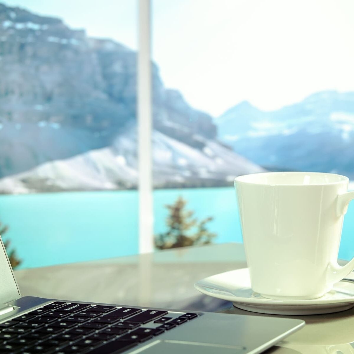 Laptop su un tavolo con una tazza e vista lago di montagna