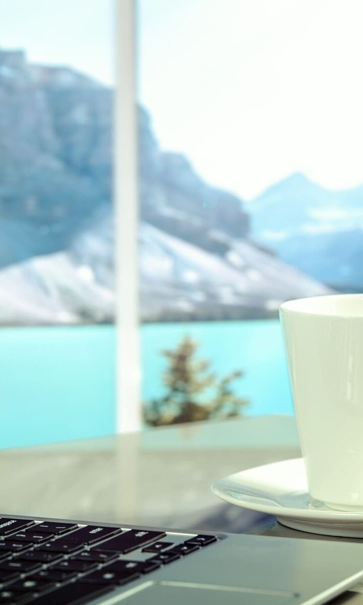 Laptop su un tavolo con una tazza e vista lago di montagna