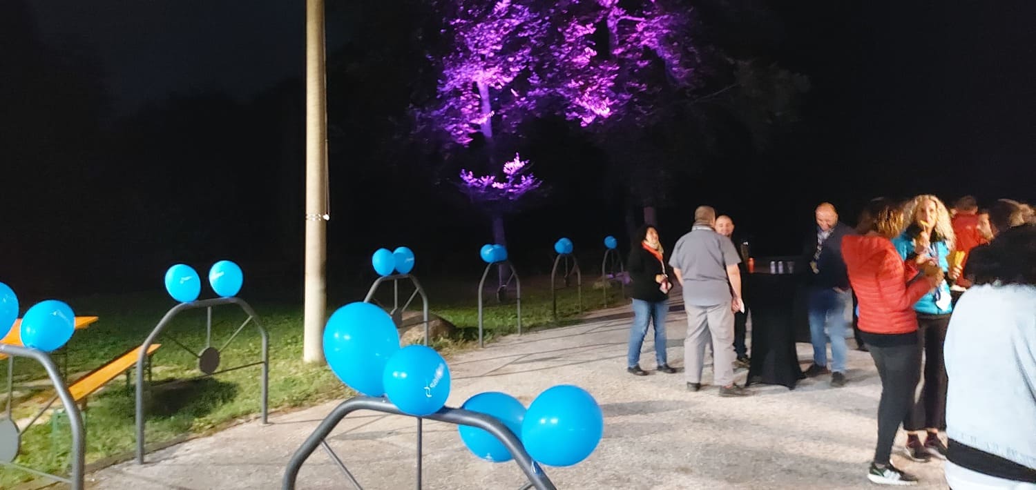 Nella notte palloncini con il marchio Saidea in primo piano, persone che bevono e mangiano e sullo sfondo un albero illuminato di viola.